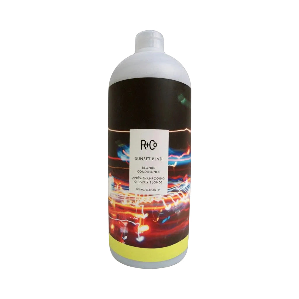 A bottle of R+Co Sunset Blonde Conditioner on a white background, featuring a black label with a colorful light streak pattern and a white cap.